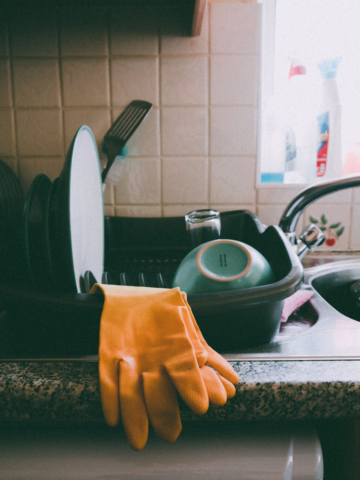 Hand-washed plates and bowls on a drying rack with rubber gloves by the sink