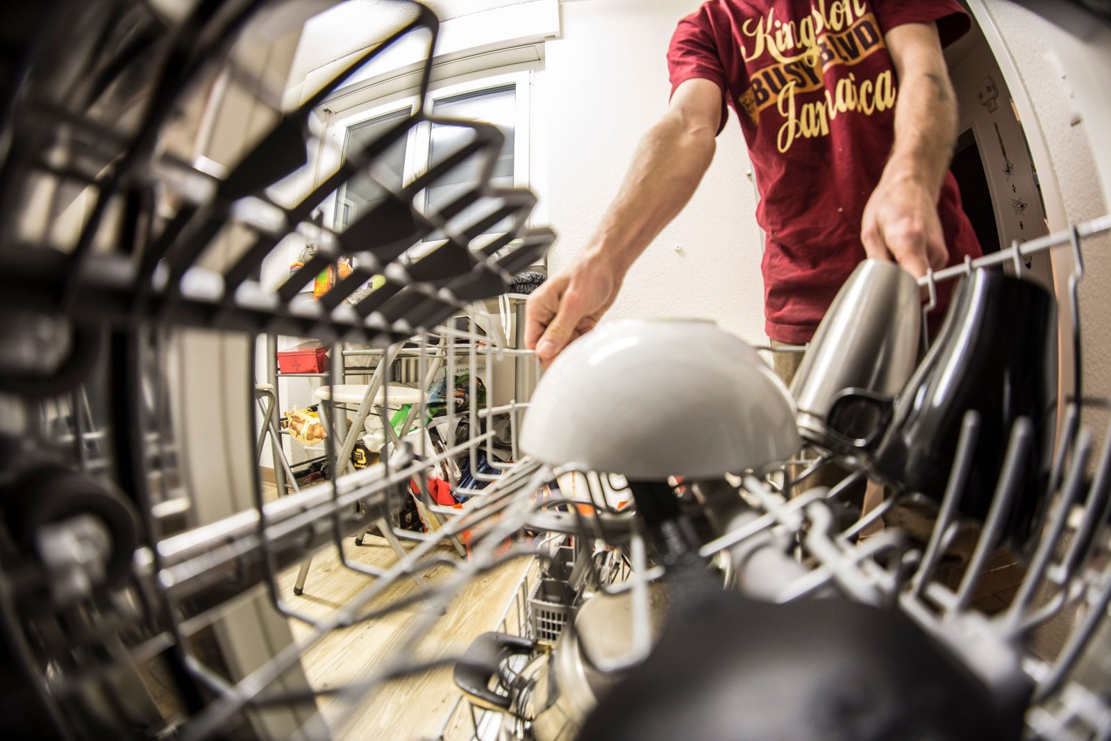 Person loading a bowl into a dishwasher upper rack, seen from inside the machine