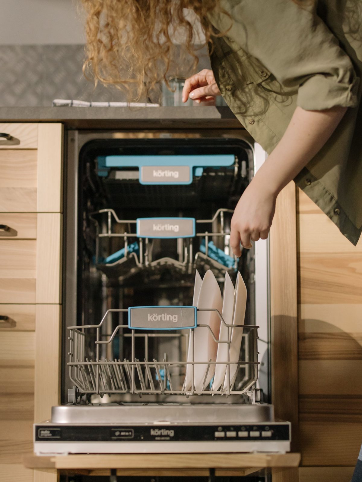 Slimline dishwasher in a light wood kitchen being loaded with plates